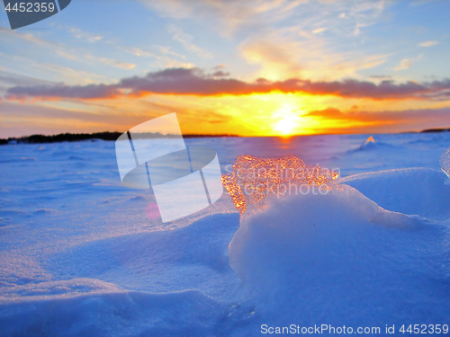 Image of Transparent piece of ice on the snow against the backdrop of a winter sunset