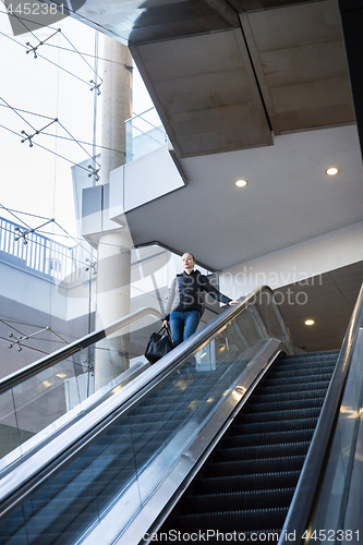 Image of Businesswoman with large black bag and mobile phone descending on escalator.