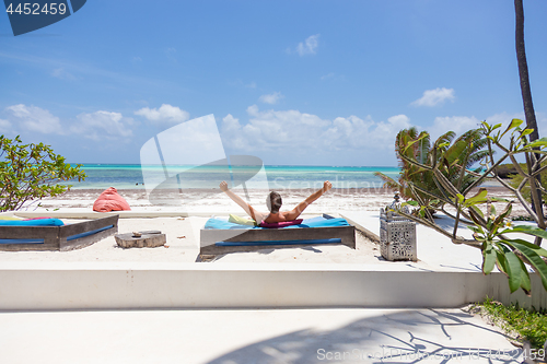 Image of Relaxed man in luxury lounger, arms rised, enjoying summer vacations on beautiful beach.