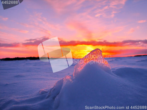 Image of Transparent piece of ice on the snow against the backdrop of a winter sunset