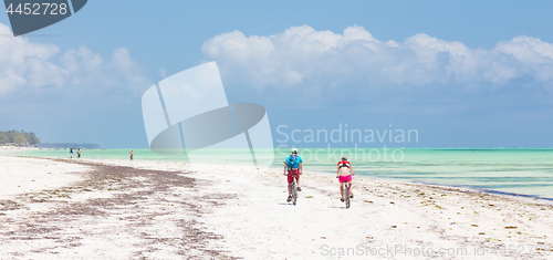 Image of Active sporty tourist couple cycling down picture perfect white sand tropical beach of Paje, Zanzibar, Tanzania.