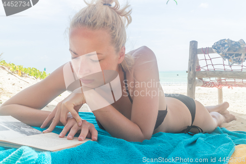 Image of Beautiful girl lying at the beach in her swimsuit and reading a book