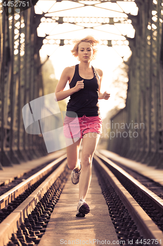 Image of Active sporty woman running on railroad tracks.