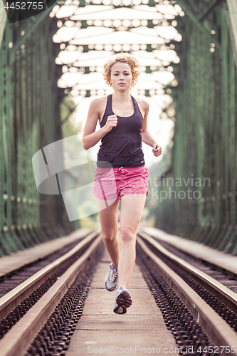 Image of Active sporty woman running on railroad tracks.