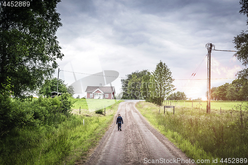 Image of Young boy walking down a road in rural environment