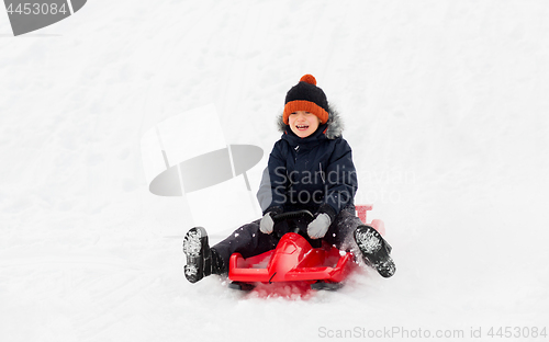 Image of happy boy sliding on sled down snow hill in winter