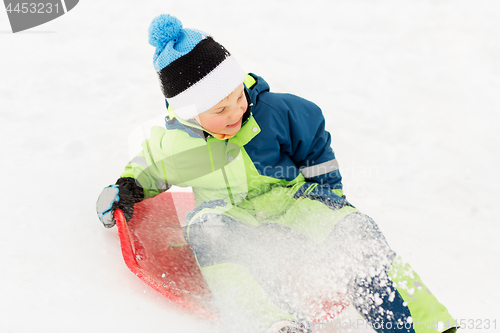 Image of happy boy sliding on sled down snow hill in winter