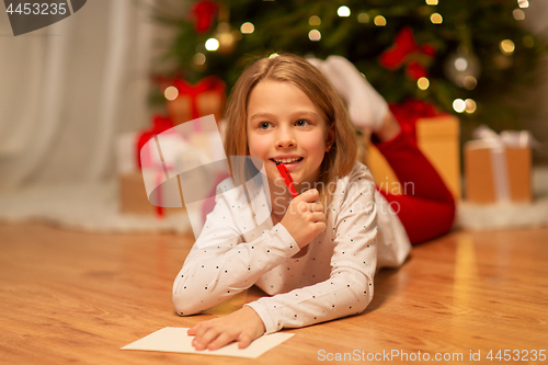 Image of smiling girl writing christmas wish list at home