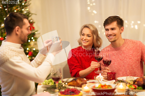 Image of happy friends photographing at christmas dinner