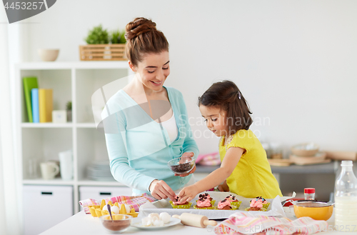 Image of happy mother and daughter cooking cupcakes at home