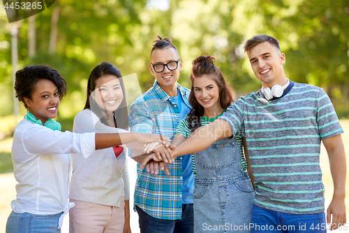 Image of happy smiling friends stacking hands in park