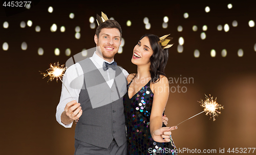 Image of happy couple with crowns and sparklers at party