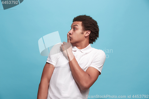 Image of The young man whispering a secret behind her hand over blue background