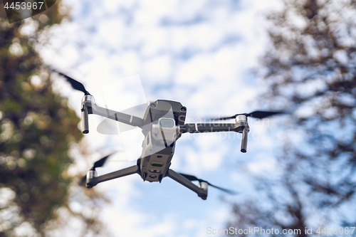 Image of Drone flying in the air, visible trees and blue sky above