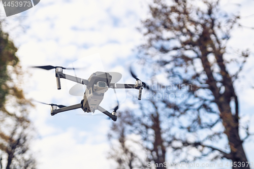 Image of Drone flying in the air, visible trees and blue sky above