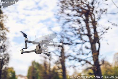 Image of Drone flying in the air, visible trees and blue sky above