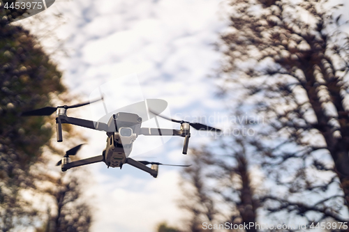 Image of Drone flying in the air, visible trees and blue sky above