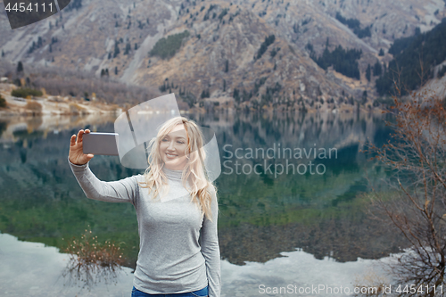 Image of Smiling woman makes selfie at the mountain lake