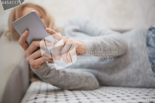 Image of Woman with smartphone laying on a sofa