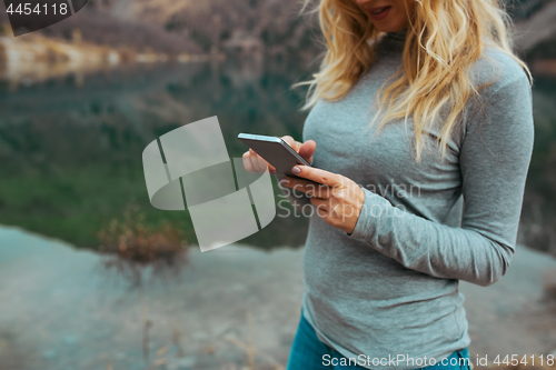 Image of Woman using smartphone at the lake