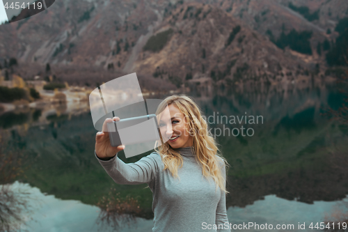 Image of Smiling woman makes selfie at the mountain lake