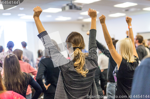 Image of Participants of interactive motivational speech feeling empowered and motivated, hands raised high in the air.