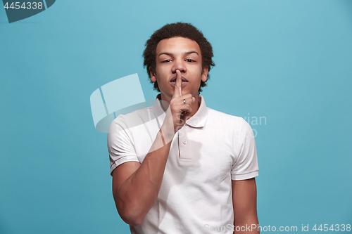 Image of The young man whispering a secret behind her hand over blue background