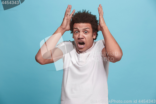 Image of The young emotional angry man screaming on blue studio background