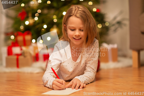 Image of smiling girl writing christmas wish list at home