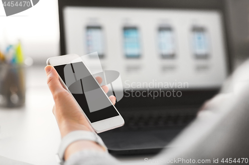 Image of web designer with smartphone and laptop at office