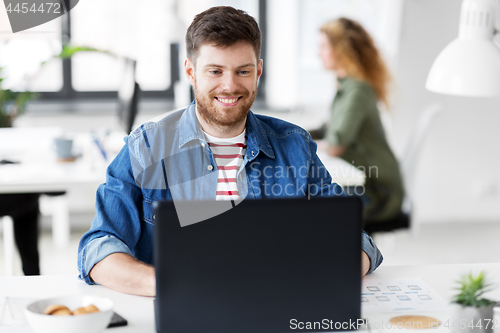 Image of smiling creative man with laptop working at office