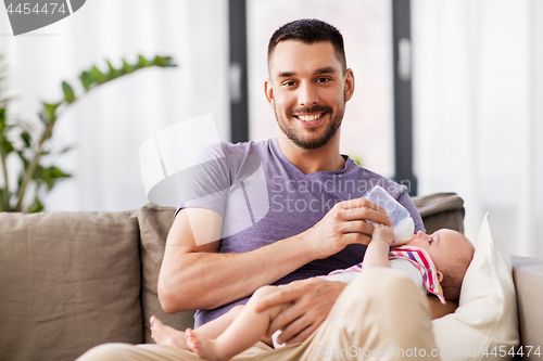 Image of father feeding baby daughter from bottle at home