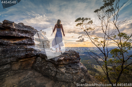 Image of Standing on a cliff edge with dress blowing in the wind she dreams