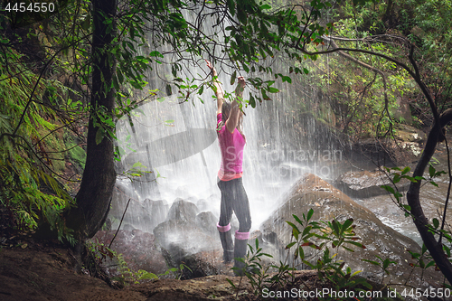 Image of Female standing in waterfalls with lush ferns, trees in bushland