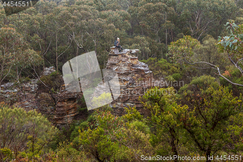 Image of Adventurous female hiker climbed up onto rocky tower in mountain bushland