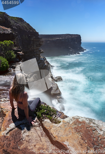 Image of Woman watches waterfall flows off cliffs into ocean