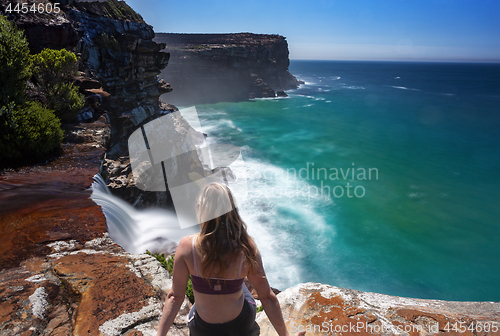 Image of Female on edge watching waterfalls flow into the ocean