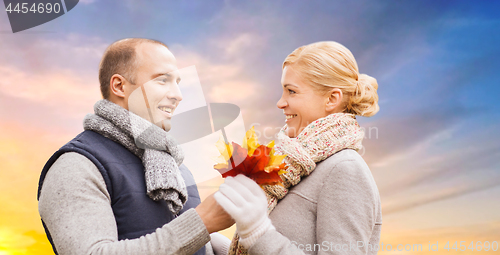 Image of couple with maple leaves over sunset sky in autumn