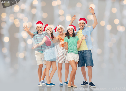 Image of happy friends in santa hats over festive lights