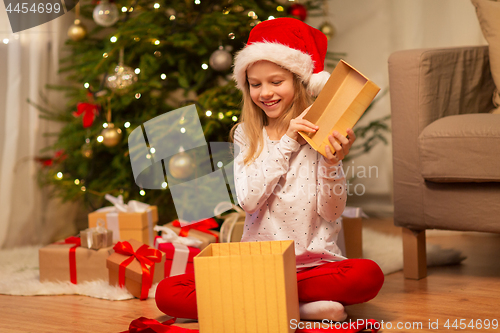 Image of smiling girl in santa hat opening christmas gift