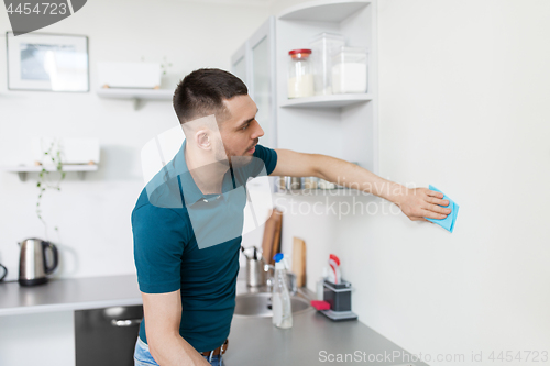 Image of man with rag cleaning wall at home kitchen