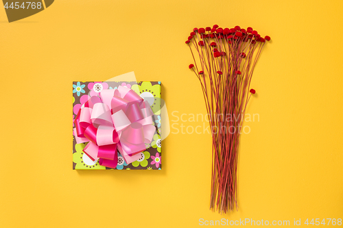 Image of Bright gift box and red flowers on yellow background