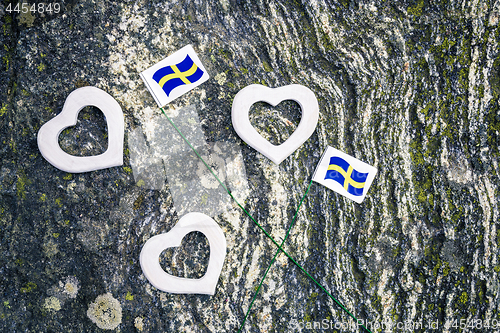 Image of Swedish flags and white hearts on mossy rock background