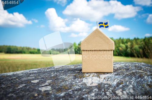 Image of Cardboard house with Swedish flag on a mossy rock