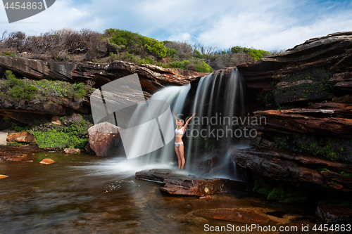 Image of Happy woman standing under a waterfall in bushland wilderness