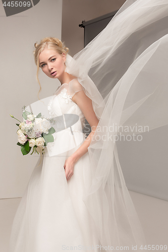 Image of Bride in beautiful dress standing indoors in white studio interior like at home. Trendy wedding style shot. Young attractive caucasian model like a bride tender looking.