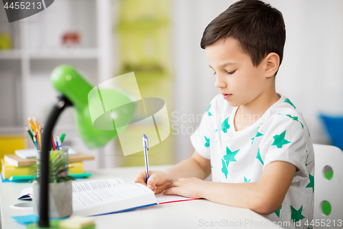 Image of boy with book writing to notebook at home