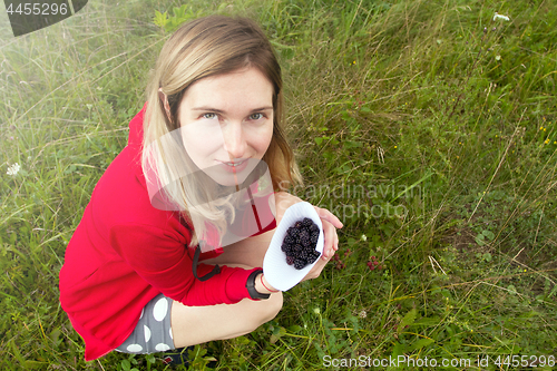 Image of Woman collecting blackberry in the meadow. Happy woman and wild 