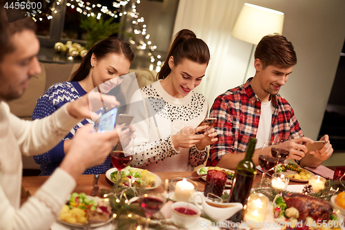 Image of friends with smartphones having christmas dinner