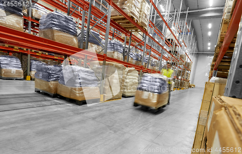 Image of worker carrying loader with goods at warehouse